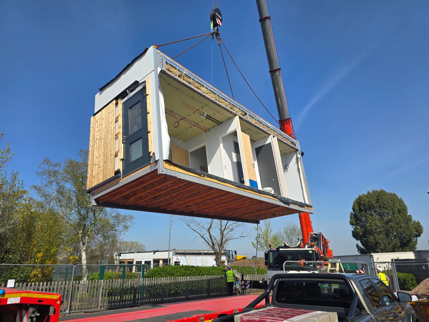 Modular building section being lifted into place by a crane on a construction site, showcasing modern off-site construction methods for fast and efficient school or commercial building installation.