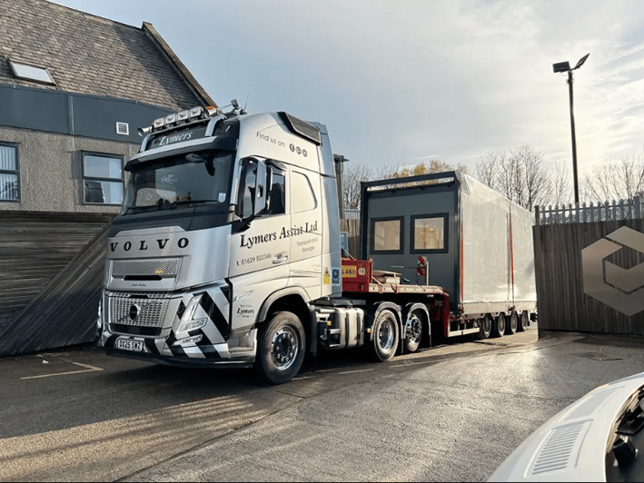 Low loader lorry transporting a permanent modular building from Elite Systems to site before crane installation, demonstrating efficient offsite modular construction and project delivery.