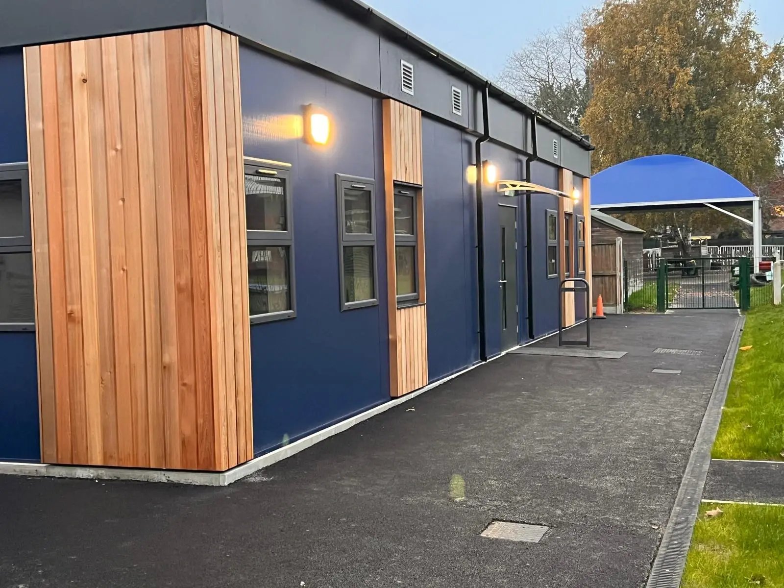Side elevation of a permanent modular classroom building featuring blue composite cladding, timber detailing and an accessible entrance at Broomgrove Infant & Junior School.