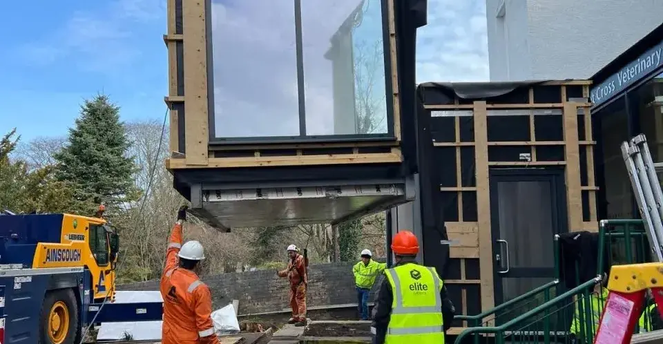 Crane installing modular building unit while workers guide placement at commercial construction site.