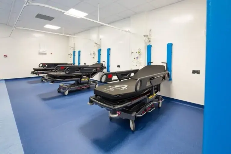 Modular Clinical room with blue flooring and white walls, featuring two black wheeled stretchers