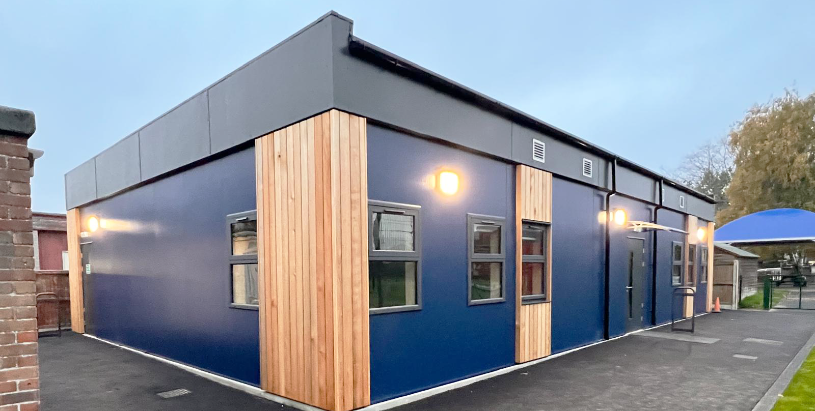Permanent modular school classroom building with blue exterior cladding, timber feature panels and level access entrance.