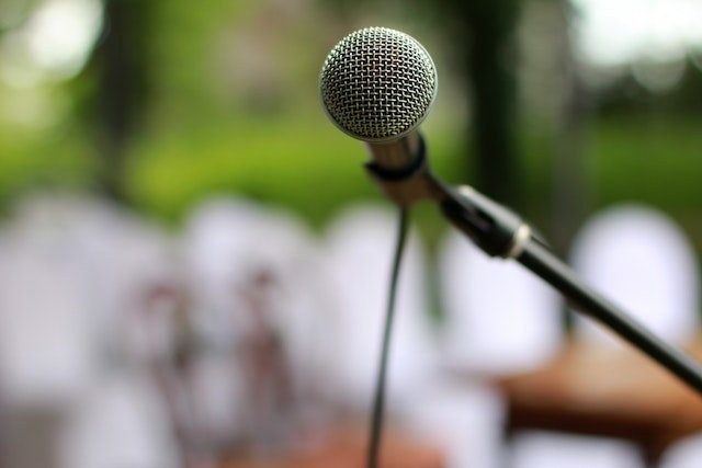 Microphone on stand with blurred background made of browns, greens and whites implying it's outside.