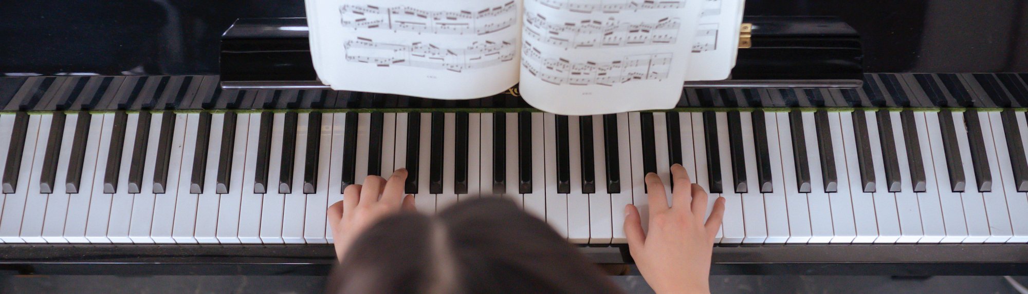 Student practicing on piano with sheet music to follow
